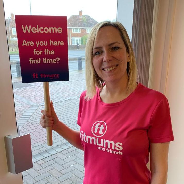 A Fitmums volunteer smiles and holds a paddle that says: Welcome - are you here for the first time?